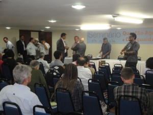 O ministro Gilberto Carvalho, falando ao microfone. À esquerda, sentado, com a mão no rosto, Pedro Stédile líder do MST