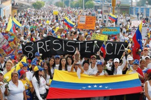 Opositores carregam uma imagem de Nossa Senhora do Carmo durante manifestação de protesto contra Maduro e sua repressão ditatorial. À esquerda, jovem com máscara contra bombas de gás lacrimogêneo.